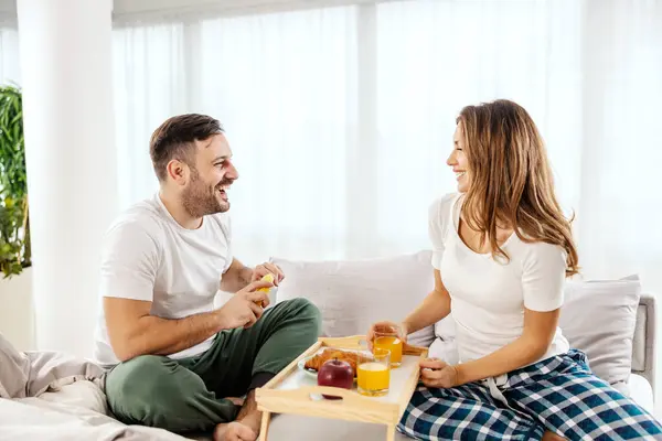 A couple in love is sitting in a bed and enjoying breakfast.