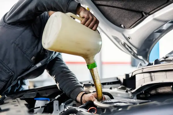 Close up picture of a mechanic pouring oil in engine under the hood while standing at mechanic\'s workshop.