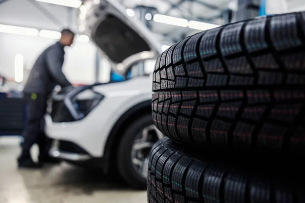 Close up of a new tires in foreground with worker fixing car in blurry background at mechanic\'s shop.