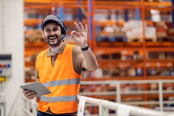 Smiling storage supervisor is gesturing okay sign for excellent organization in logistics.