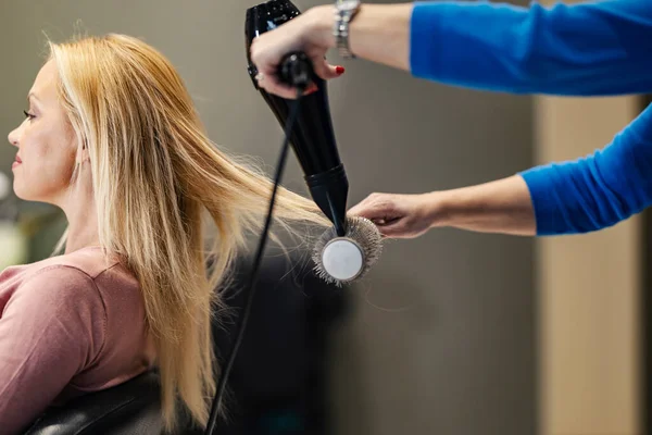 Cropped picture of a hair stylist styling client\'s hair in a salon.