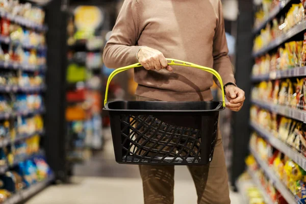 Cropped picture of a senior man with shopping basket purchasing at the hypermarket.