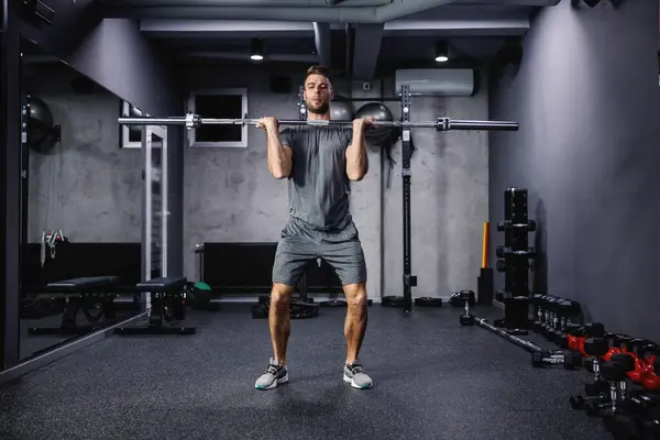Cross fit training with barbell lifting. An attractive and muscular man. A man in sportswear pumps his arm muscles and lifts a barbell in a modern gym. Copy space for marketing massage