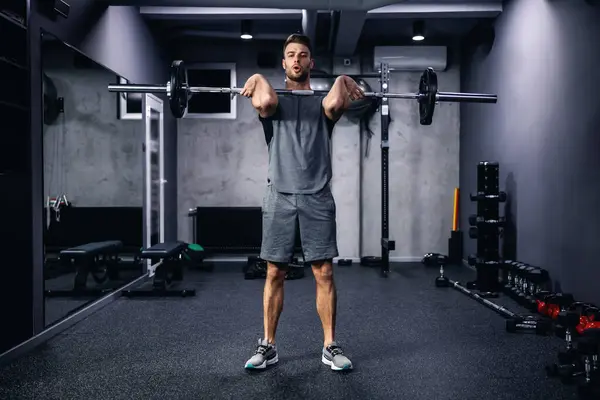 A man exercising with a barbell gym. A photo of a young sexy man in sportswear and good physical shape in an isolated indoor gym. Strength and motivation, sports, fitness goal, personal training