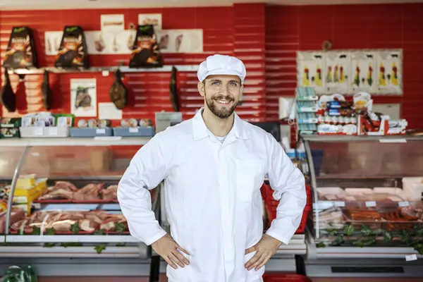 成功した肉屋の労働者が店に立ってカメラで微笑んでいる ストックフォト