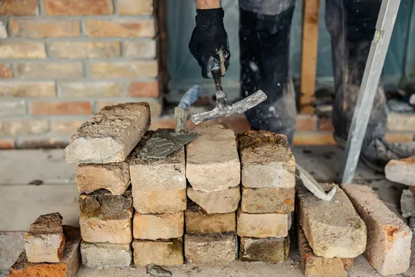 A housebuilder\'s hand taking tools from a pile of bricks.