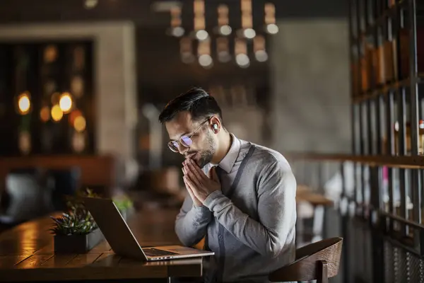 一位穿着时髦休闲装的年轻商人坐在咖啡店里一边看着笔记本电脑一边祈祷 — 图库照片