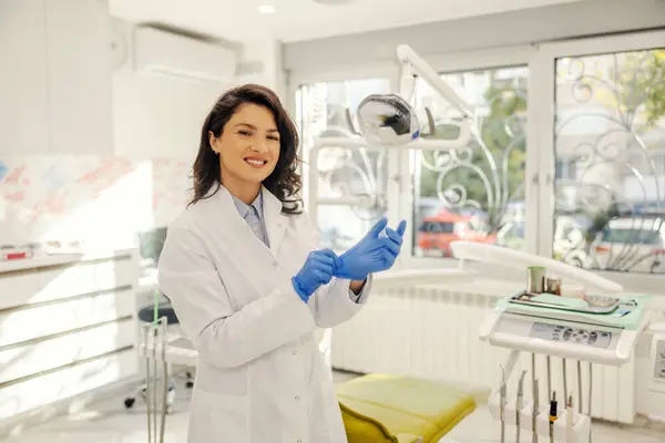 歯医者オフィスに立って笑顔で手袋を置く幸せな歯科医の肖像画 — ストック写真