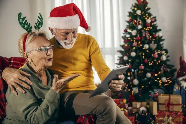 A senior couple having video call on tablet at home with family and sending kisses on christmas and new year.
