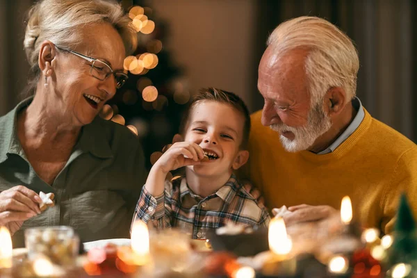 A happy grandparents having fun with grandchild who is eating cookie at christmas and new year\'s eve at home at christmas table.