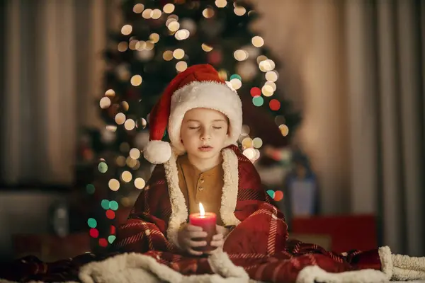 圣诞节和新年前夕 一个眼睛闭着的可爱的小男孩正坐在家里 一边举着蜡烛一边许愿 — 图库照片