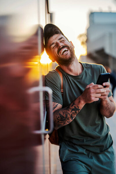 A man with phone is laughing while leaning on the wall on the city street. — Stock Image Man Phone Laughing While Leaning Wall City Street Stock Image