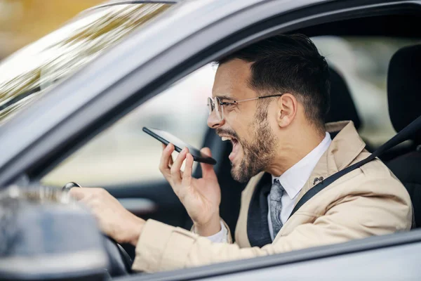 怒った若いエレガントなエグゼクティブは 電話に怒った声のメッセージを残しながら彼の車を運転しています — ストック写真