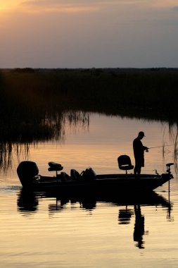 Silhouette of man fishing off of a boat at sunset