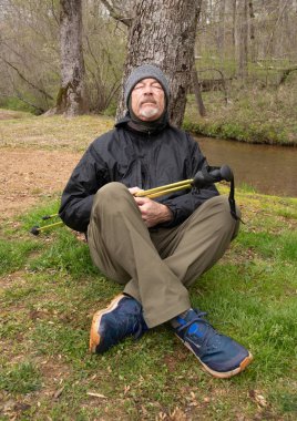 Yaşlı yürüyüşçü ormanda bir günlük yürüyüşten sonra bir ağaca karşı dinleniyor.