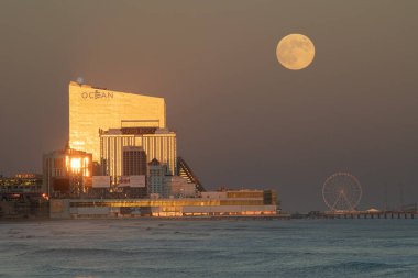 Atlantic City, New Jersey 'de dolunay doğuyor ve batan güneş kumarhanelere yansıyor. Önplanda okyanus
