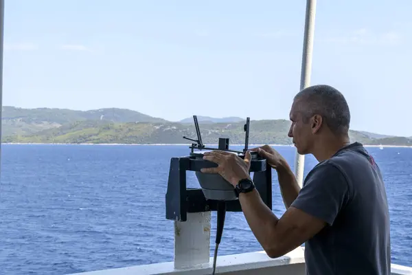 Navigational officer taking bearing with azimuth ring on gyro compass on the wing of navigational bridge. Navigational equipment usage. Observations.
