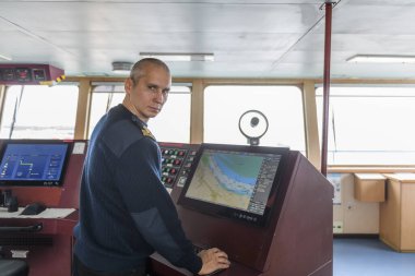 Officer on watch with electronic chart on the navigational bridge. Caucasian man in blue uniform sweater using ECDIS on the bridge of cargo ship. clipart