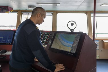 Seyir köprüsünde elektronik çizelgeyle nöbet tutan bir memur var. Mavi üniformalı beyaz adam kargo gemisinin köprüsünde ECDIS kullanıyor..