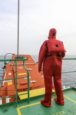 Seaman wearing Immersion Suit on Muster station. Abandon ship drill. Free fall boat. Cargo vessel. clipart