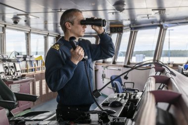 Seyir köprüsünde dürbünlü bir güverte subayı. Gemide denizci var. Ticari nakliye. Kargo gemisi.