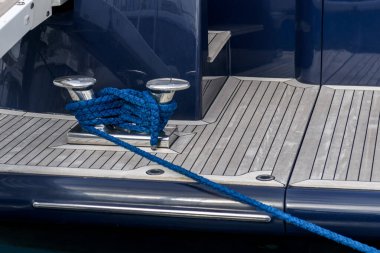 Süper yat güvertesinde mavi ipli paslanmaz çelik krampon. Süper yatın güvertesine bağlanmış demirleme halatı. Bağlanma düzenlemeleri.