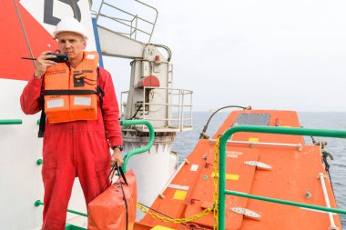 Muster istasyonunda Vhf radyosu olan can yeleği giyen denizci. Tatbikatı terk edin. Serbest düşüş teknesi. Kargo gemisi.