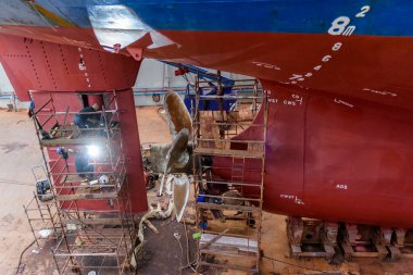 Gemi tamirhanesindeki kargo gemisi kuru rıhtımda. Değişken pervane ve dümen. Geminin tamirhanesinde çalışan kaynakçı..