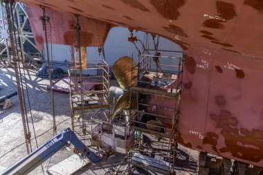 Gemi tamirhanesindeki kargo gemisi kuru rıhtımda. Değişken pervane ve dümen. Geminin tamirhanesinde çalışan kaynakçı..