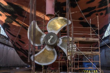 Gemi tamirhanesindeki kargo gemisi kuru rıhtımda. Değişken pervane ve dümen. Geminin tamirhanesinde çalışan kaynakçı..