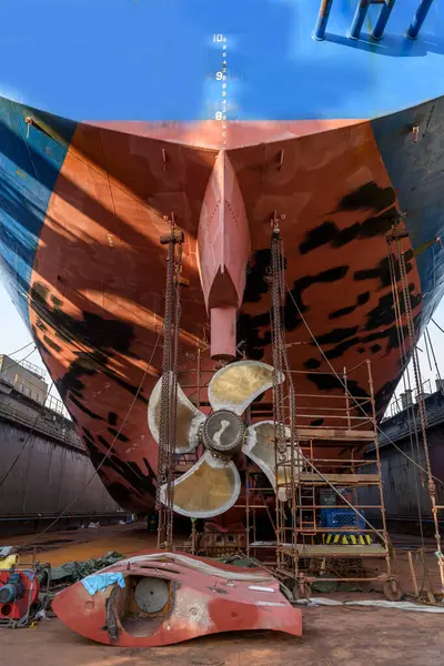 Gemi tamirhanesindeki kargo gemisi kuru rıhtımda. Değişken pervane ve dümen. Geminin tamirhanesinde çalışan kaynakçı..