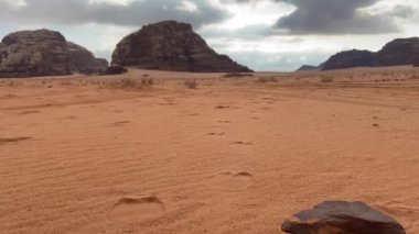 Ürdün 'deki Wadi Rum Çölü' nün panoramik manzarası. Arkaplanda dağlar olan düz kum üzerinde hareket eden bulutlar.,