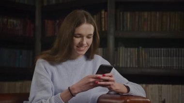 Woman typing on smartphone indoors. Smiling 20s caucasian female texting on her smart phone.