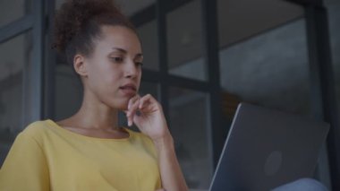 Woman evaluating job offer. Thoughtful lady reading on laptop indoors in loft office