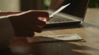 Handheld closee up of caucasian woman hands counting money in front of laptop computer in slow motion