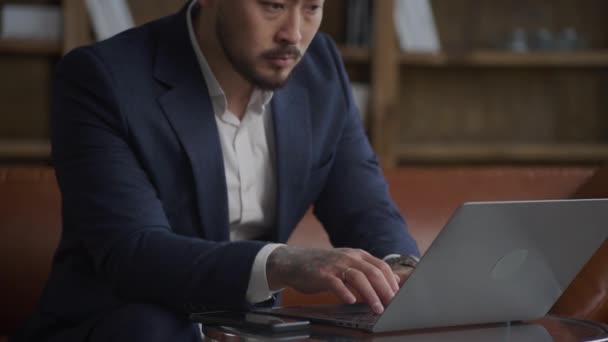 ノートパソコンに入力するビジネスマン 彼のコンピュータ上でオフィスで働く人に焦点を当てました 大人アジアの入れ墨男身に着けています彼の仕事に集中しています屋内 — ストック動画