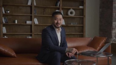 Modern Asyalı İşadamı Portresi Ofiste. Yetişkin bir adam takım elbise giyiyor ve ağır çekimde el kamerasına bakıyor.