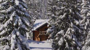 Forest cabin covered in snow on sunny winter day in mountains. Slow optical zoom out from a wooden house in woods