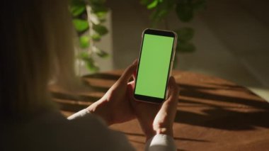 Unrecognizable woman holding smartphone with green screen chroma key in bright sunlight