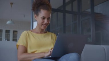 Woman working on a laptop with smile. Young African American female typing on computer indoors - low angle shot