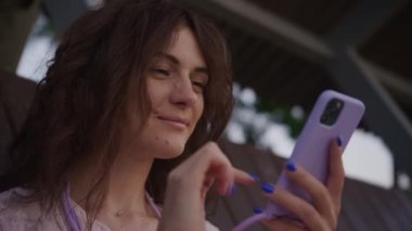 Youth browsing on smartphone, young woman using smart phone. Curly caucasian student surfing online outside in slow motion