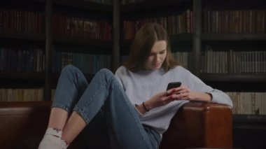 Genç bir kadın kapalı alanda akıllı telefon kullanarak internette geziniyor. Beyaz kadın internette sörf yapıyor.