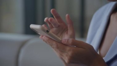 Kadın elleri akıllı telefonda geziniyor. Çok yakından. Parmaklarıyla kaydırıp, kaydırıyor ve takım elbise giyiyor.