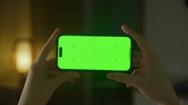 Yeşil ekranlı, yatay akıllı telefon. Beyaz kadın elleri kapalı alanda krom anahtarı olan akıllı bir telefon tutuyor.