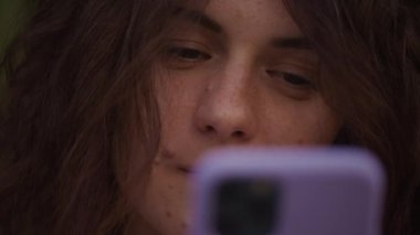 Woman eyes looking at smartphone extreme close up. Curly caucasian female browsing online in slow motion