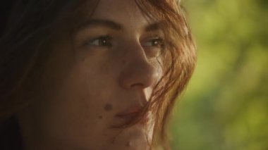 Handheld close up catching sunbeam on curly caucasian woman face with freckles and birthmark outside in slow motion