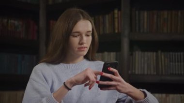 Akıllı telefonunda gezen bir kadın, internetten alışveriş yapan beyaz bir kadın. Genç yetişkin bir öğrenci kütüphanede akıllı telefonunu kullanıyor.