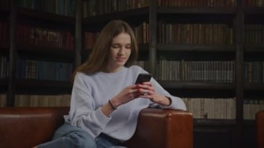 İnternette gülümseyen bir kadın, akıllı telefondan gülen bir kadın. Beyaz öğrencilerin kapalı alandaki akıllı telefonlarıyla mesajlaşmaları.
