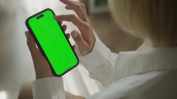 クロマキースマートフォンで手スクロール 肩のビュー上 Fpsで屋内で緑の画面のスマートフォンを使用している女性 — ストック動画