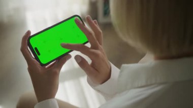 Omuz manzarası üzerinde yatay yeşil ekran akıllı telefonda el kaydırma. 60 fp içinde kapalı alanda krom anahtarı olan akıllı telefon kullanan bir kadın.